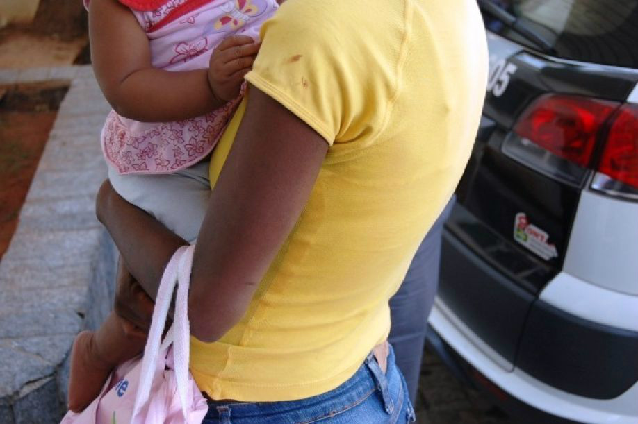 Mãe com a filha no colo na Santa Casa; manchas de sangue do nariz da criança na camiseta da mulher