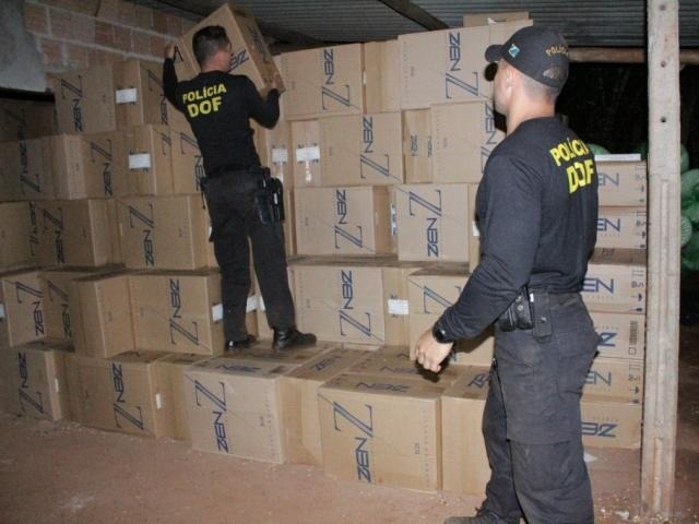 Agentes do DOF empilham caixas de cigarro encontradas em depósito de contrabandistas, em Mundo Novo. Foto: Divulgação/DOF
