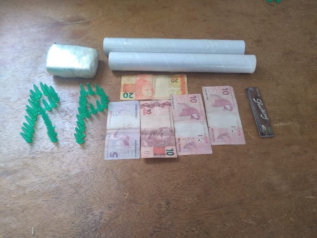 O tablete da suposta maconha, os dois rolos de papel filme, uma quantia apreendida e os 42 pinos para armazenamento de entorpecentes. Foto: Divulgação Polícia Militar