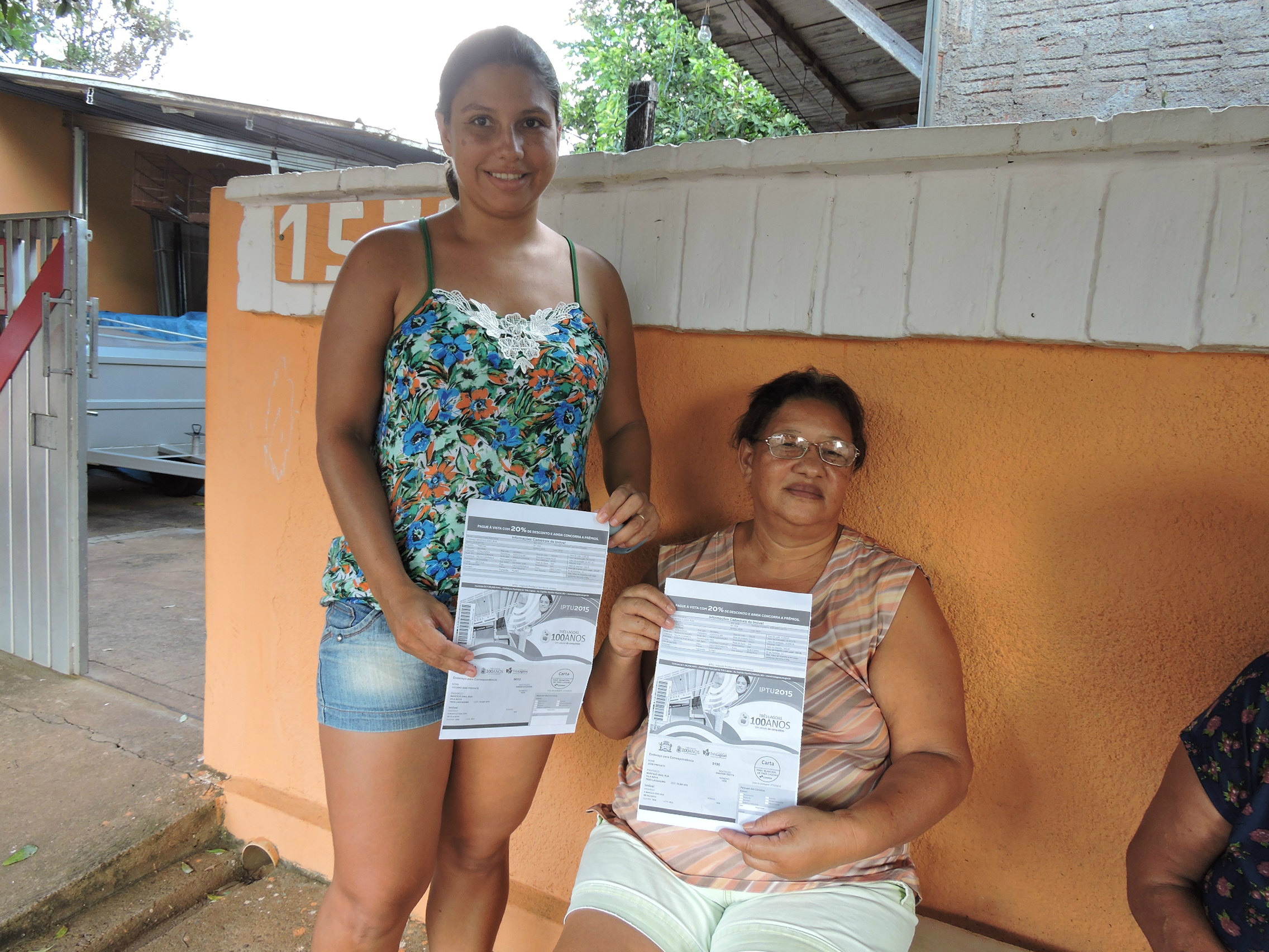 As moradoras, Andressa e Maria, apresentam os boletos do IPTU em que no primeiro consta como pavimentado e no segundo não