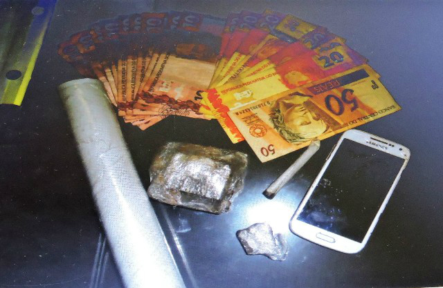 Em buscas realizadas no local, os PMs encontraram uma pequena porção de maconha embalada para a venda, um cigarro de maconha, um tablete do mesmo entorpecente enterrado no quintal, material usado para a embalagem da droga, um celular e uma quantia de R$ 270,00 em dinheiro. Foto: Rádio Caçula