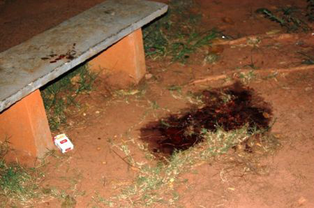 Banco da praça onde a vítima foi baleada com pelo menos dois tiros e a mancha de sangue no solo.Foto: Ata News