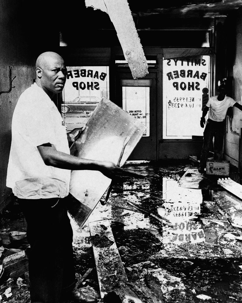 Nesta foto de arquivo de 17 de agosto de 1965, A.Z. Smith, vítima dos distúrbios de Los Angeles, verifica os danos à sua barbearia na área de Watts, em Los Angeles. Os estabelecimentos comerciais pertencentes a brancos eram os alvos habituais de saqueadores e incendiários. Smith foi um dos poucos negros apanhados na turbulência. (Foto AP)