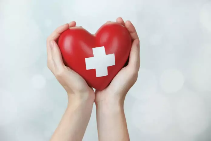 Red heart with cross sign in female hand, close-up, on light background